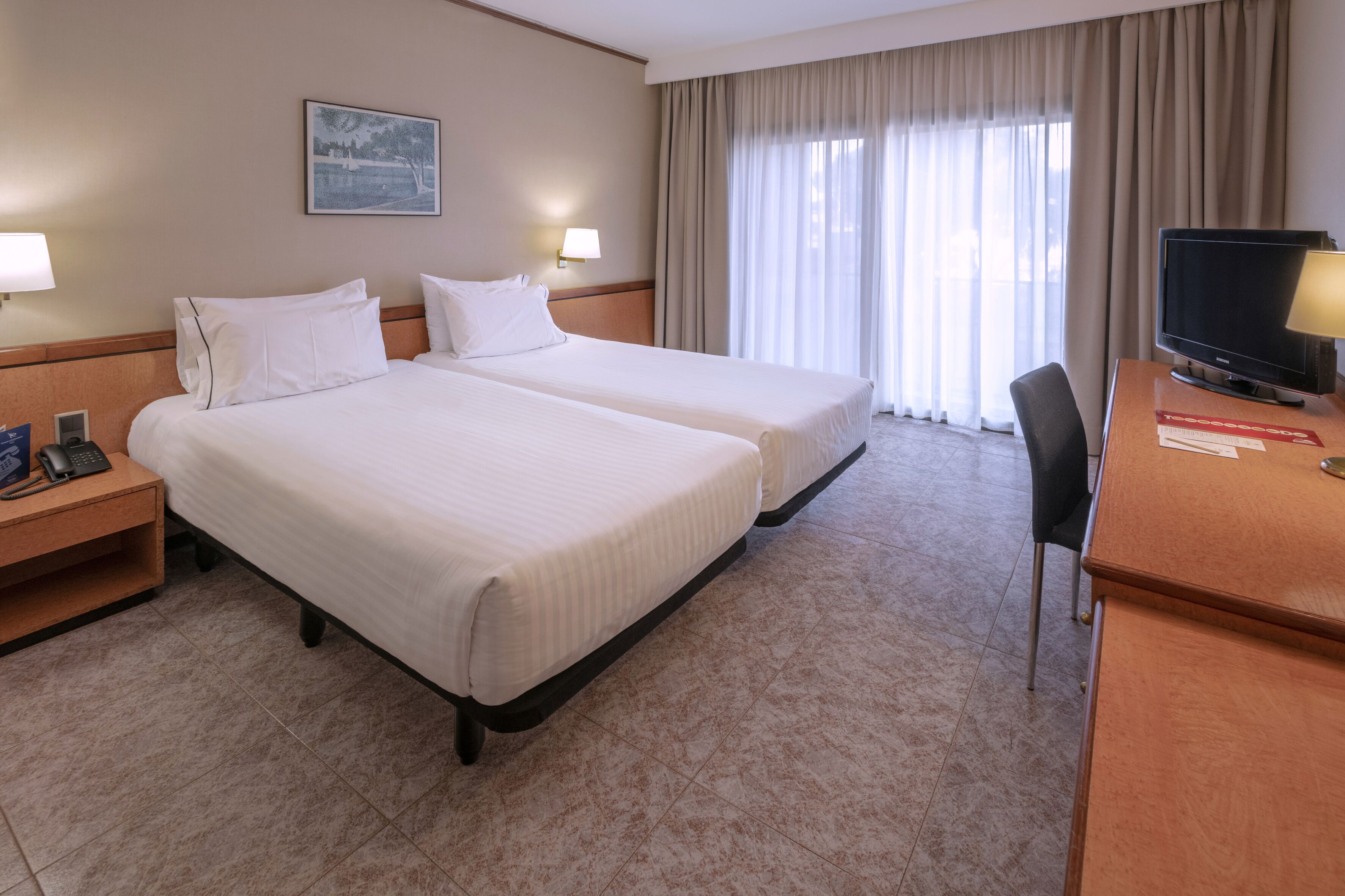 A hotel room with two beds, a desk with a television, and a window with curtains.