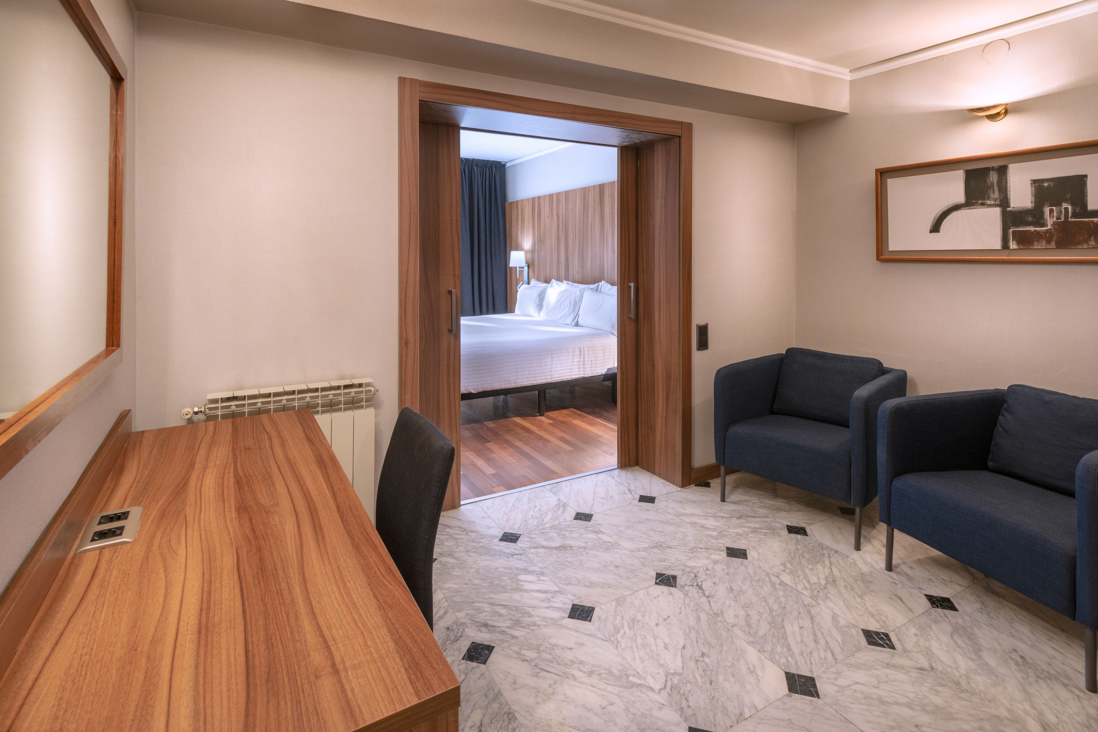 A hotel room with a wooden desk, a blue sofa, and a bed with white linens.