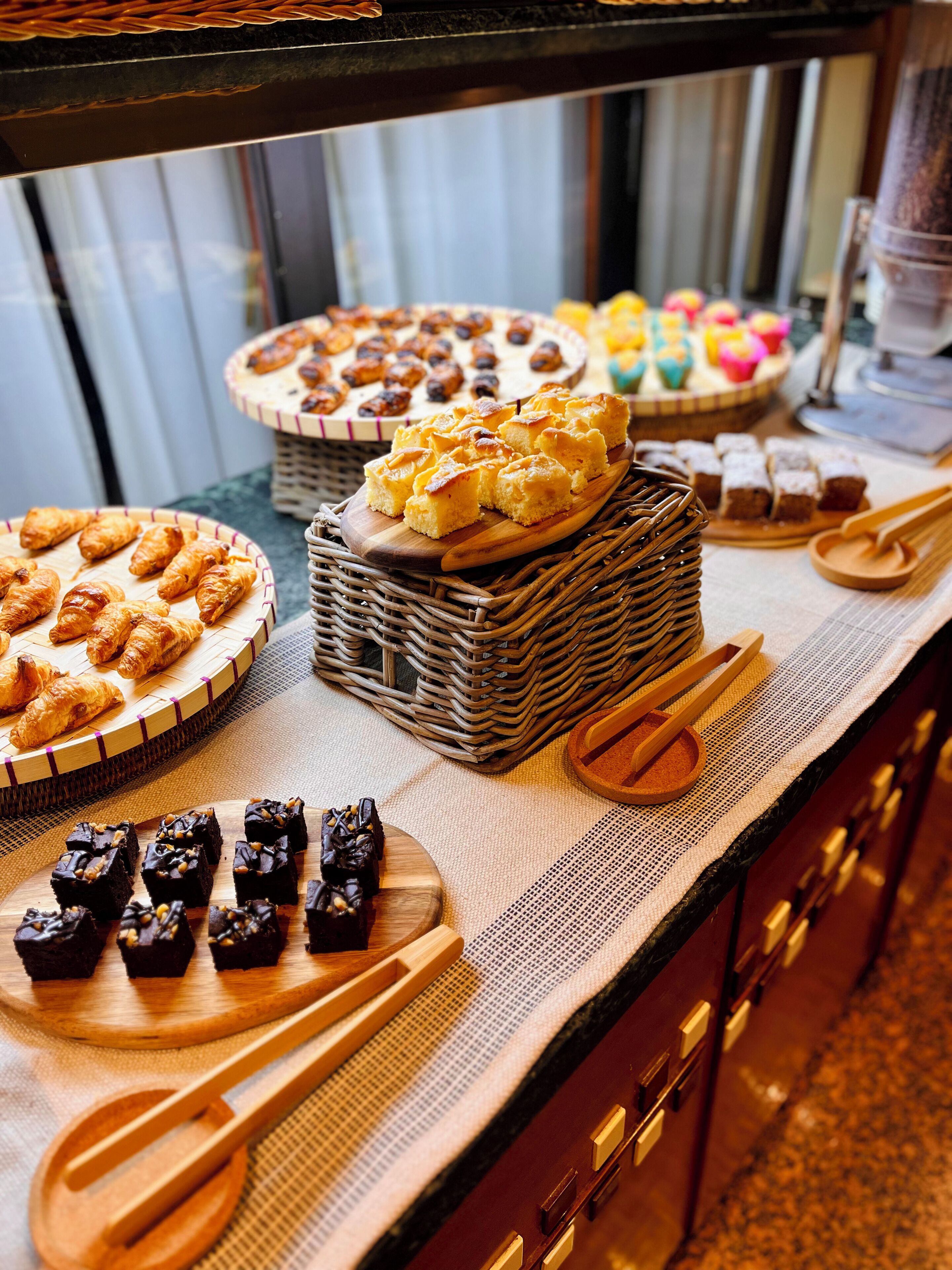 A buffet table with various baked goods, including pastries and desserts, arranged on wooden boards and baskets.