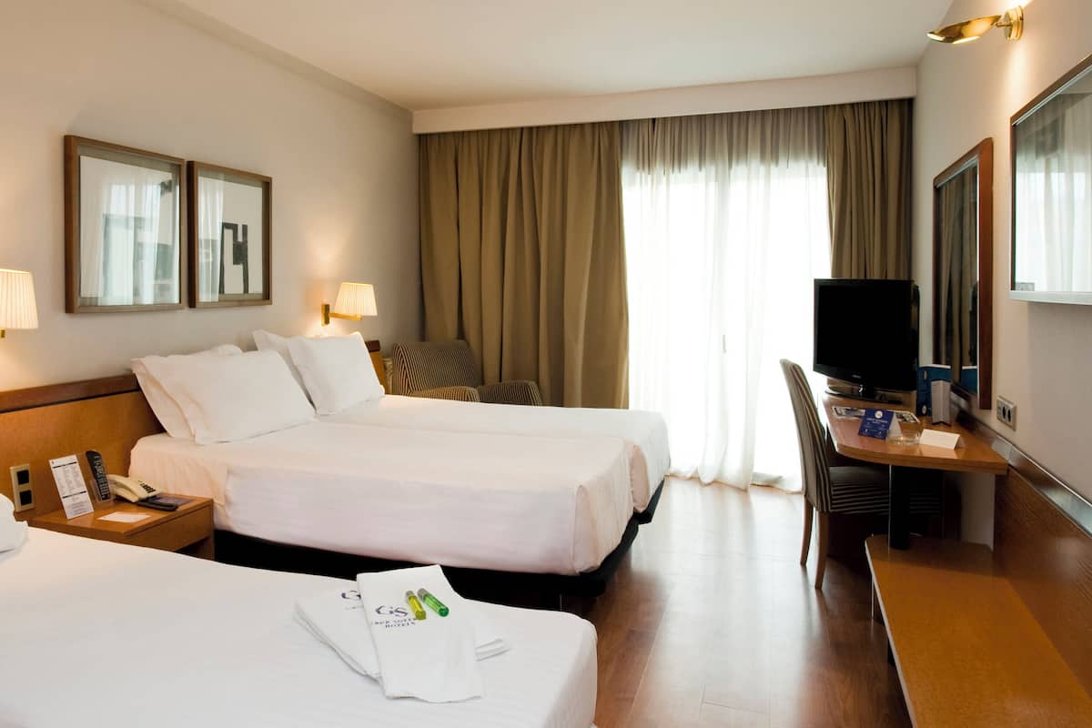 Une chambre d’hôtel avec deux lits, un bureau avec une chaise, une télévision et un miroir.