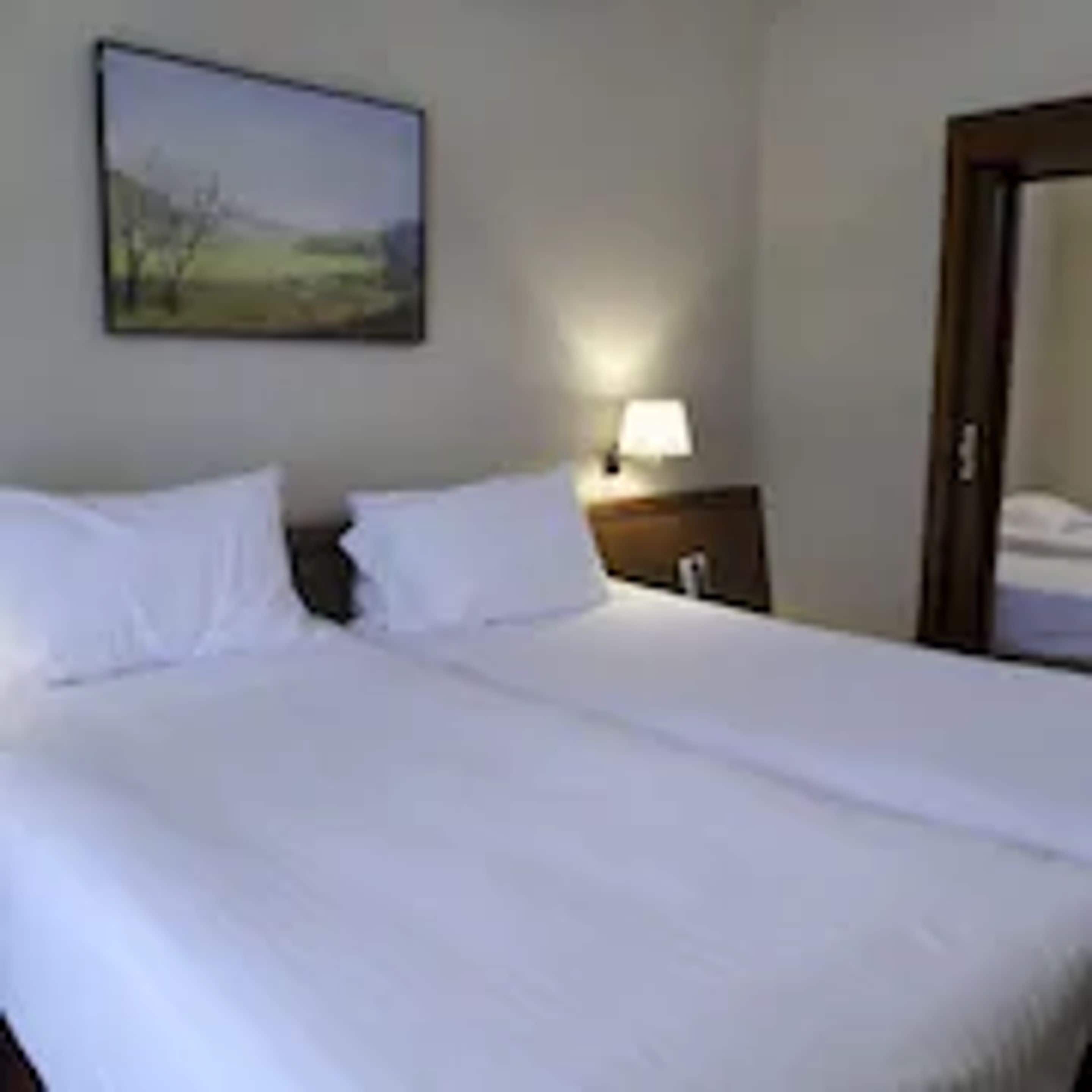 A neatly made bed with white linens in a hotel room.