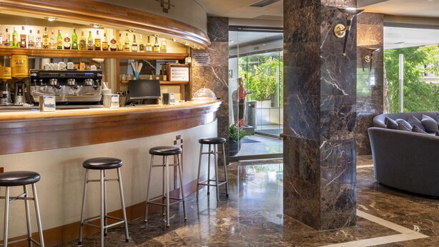 Zona de bar con una máquina de café, taburetes y una variedad de botellas.