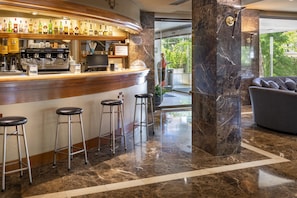 Zona de bar con una máquina de café, taburetes y una variedad de botellas.