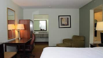 Habitación de hotel con cama, escritorio con silla, espejo, un cuadro en la pared y baño visible a través de una puerta abierta.