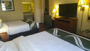 A hotel room with two beds, a television, a desk, and a chair.