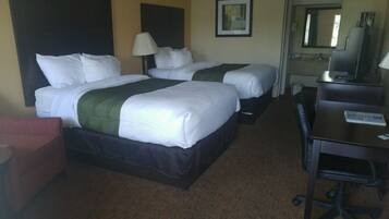 A hotel room with two beds, a desk, a chair, a lamp, and a mirror.