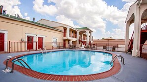 A swimming pool with a brick border, surrounded by a building with balconies and a covered seating area. - Quality Inn & Suites Covington (Covington)