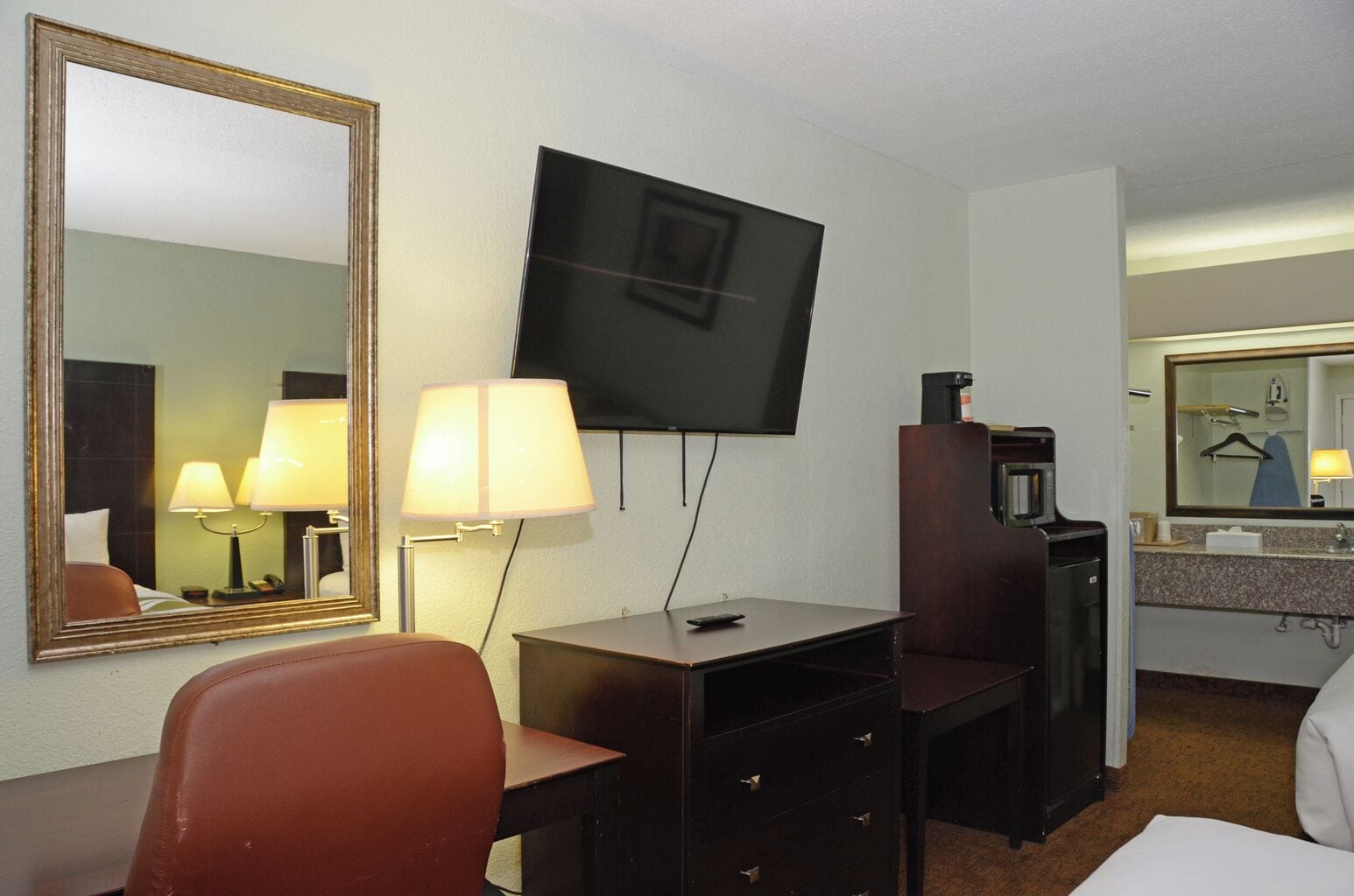 Une chambre d’hôtel équipée d’un bureau, d’une chaise, d’une télévision, de lampes et d’un miroir.
