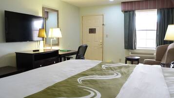Habitación de hotel con cama, escritorio, silla, televisión y ventana con cortinas.