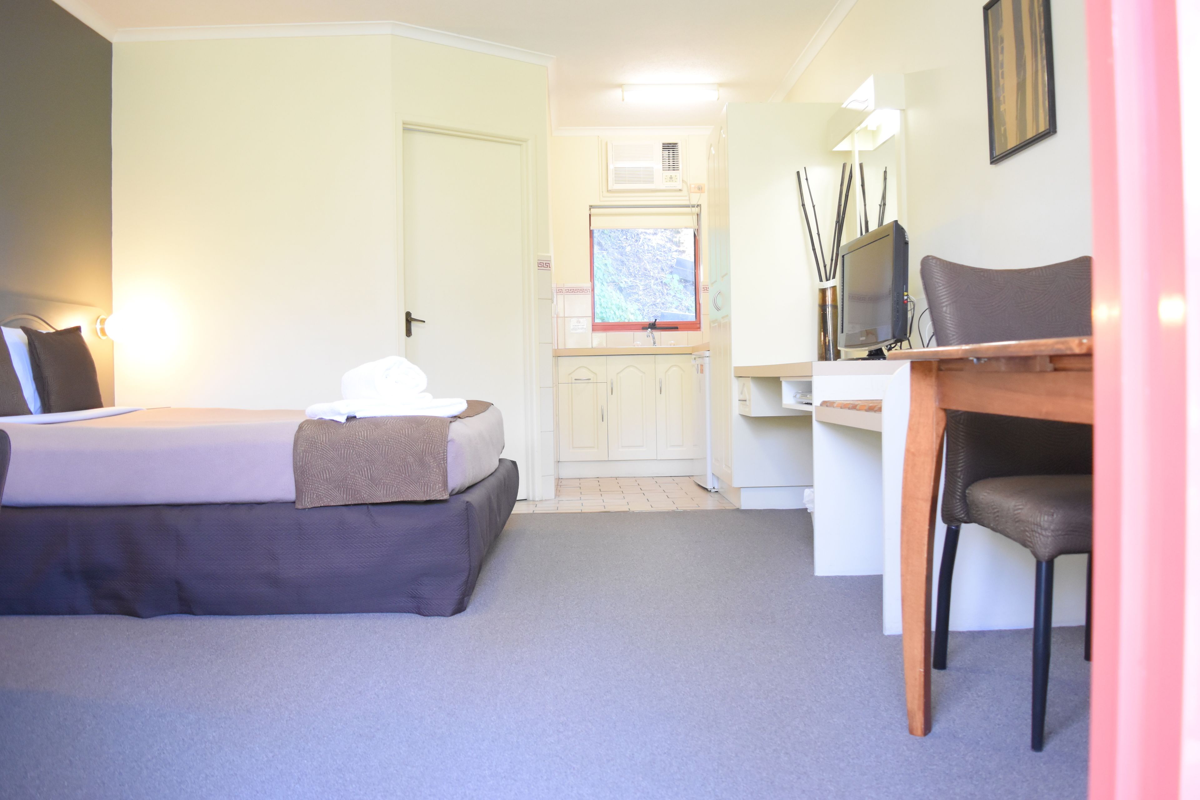 Une chambre à coucher avec un lit, un bureau et une chaise. Il y a une fenêtre donnant sur des arbres.