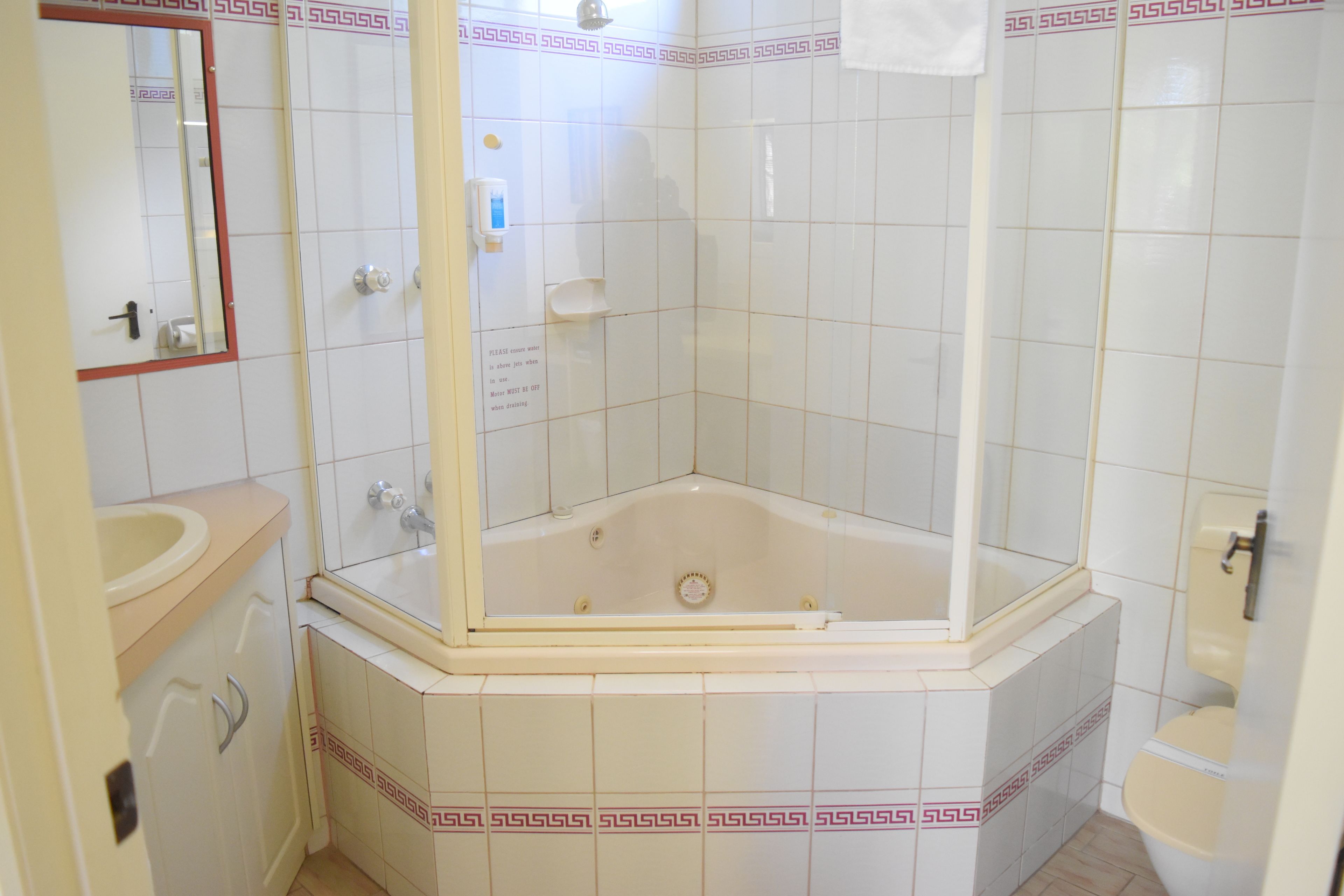 Un baño con bañera en esquina, lavamanos y retrete.