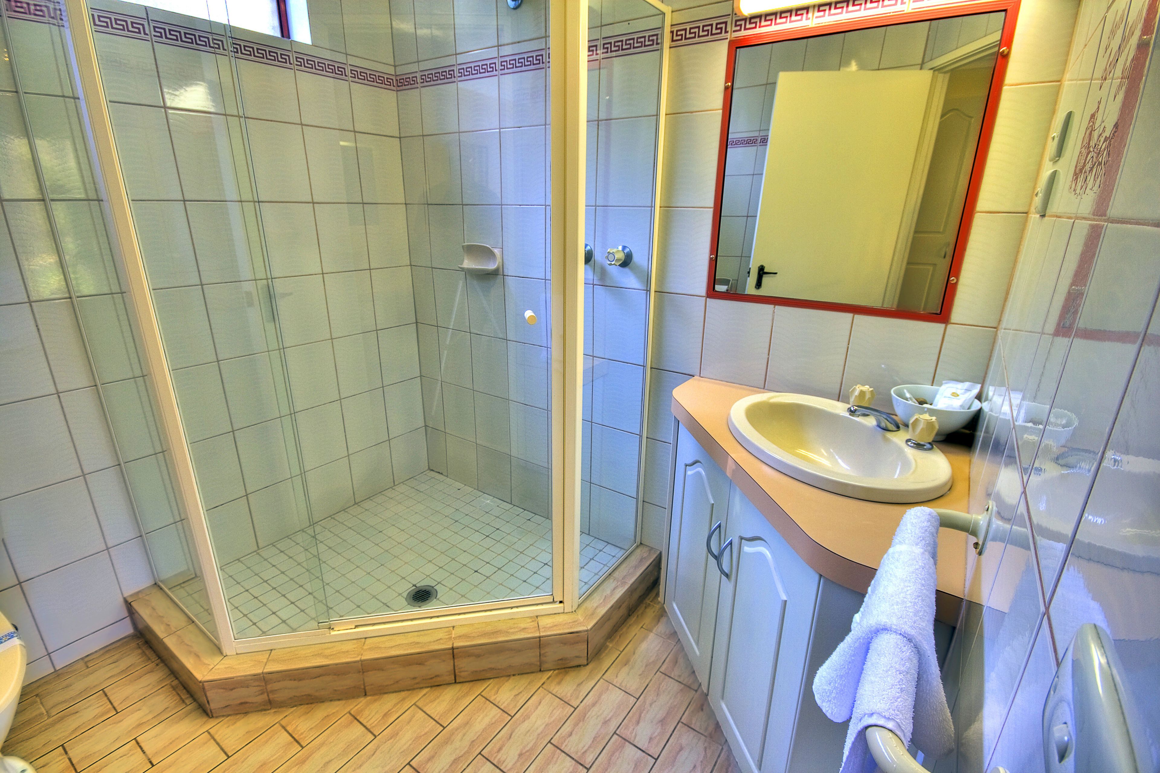 Ein modernes Badezimmer mit einer gläsernen Duschkabine, einem Waschbecken mit Spiegel und Holzboden.