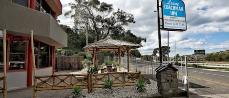 Un motel llamado 'Lorne Coachman Inn' con un letrero llamativo, un pequeño pabellón y un camino pavimentado.
