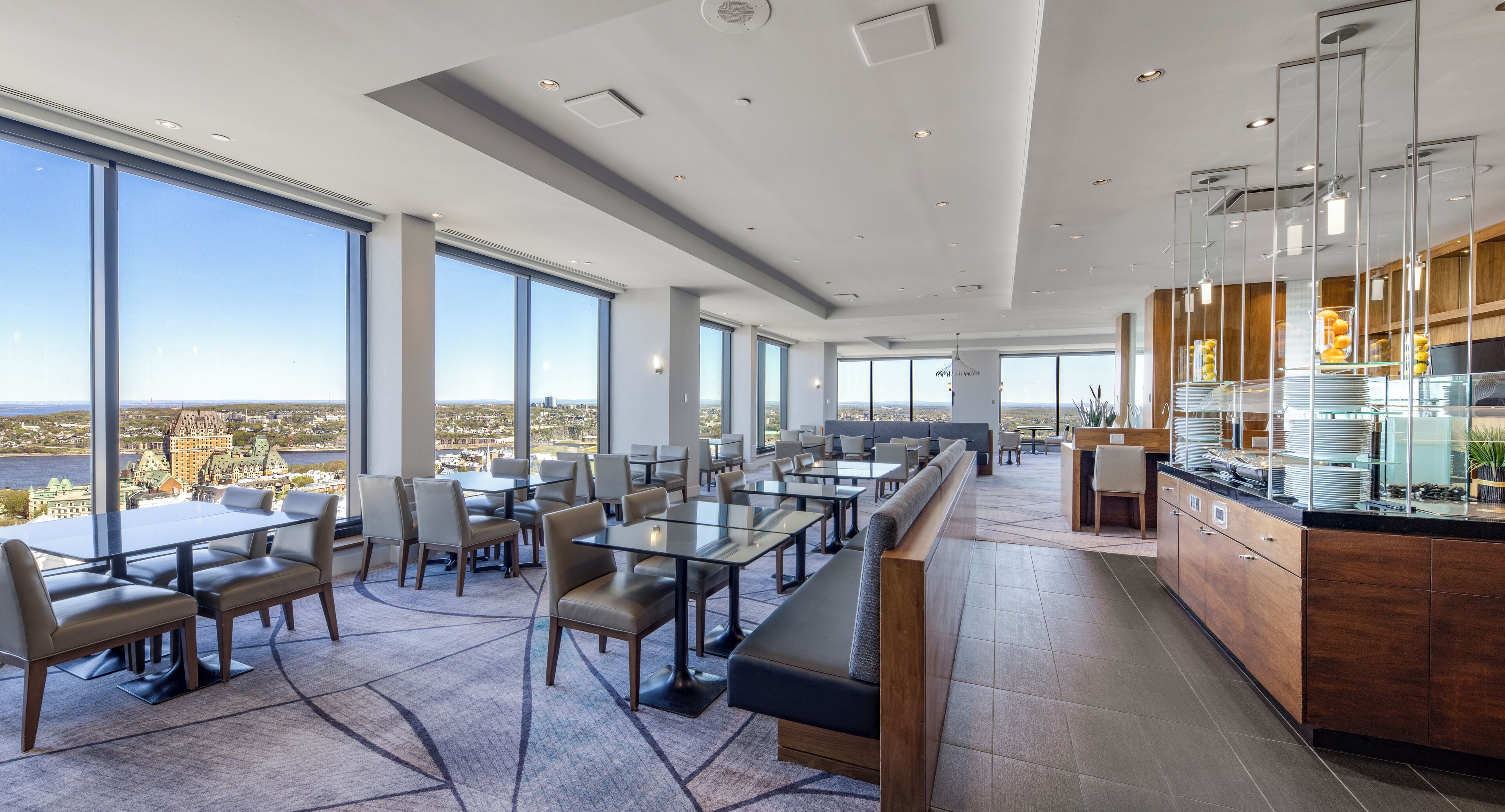 A modern dining area with large windows, tables, and a kitchen counter.