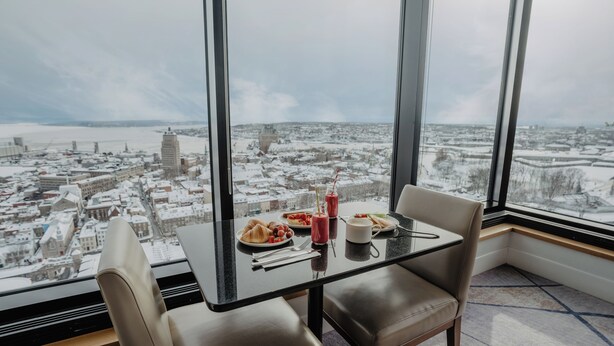A high-rise room with a city view, a table with breakfast, and large windows.
