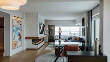 A modern living room with a fireplace, a large window with a city view, a dining area with a glass table, and a seating area with a sofa and chairs.