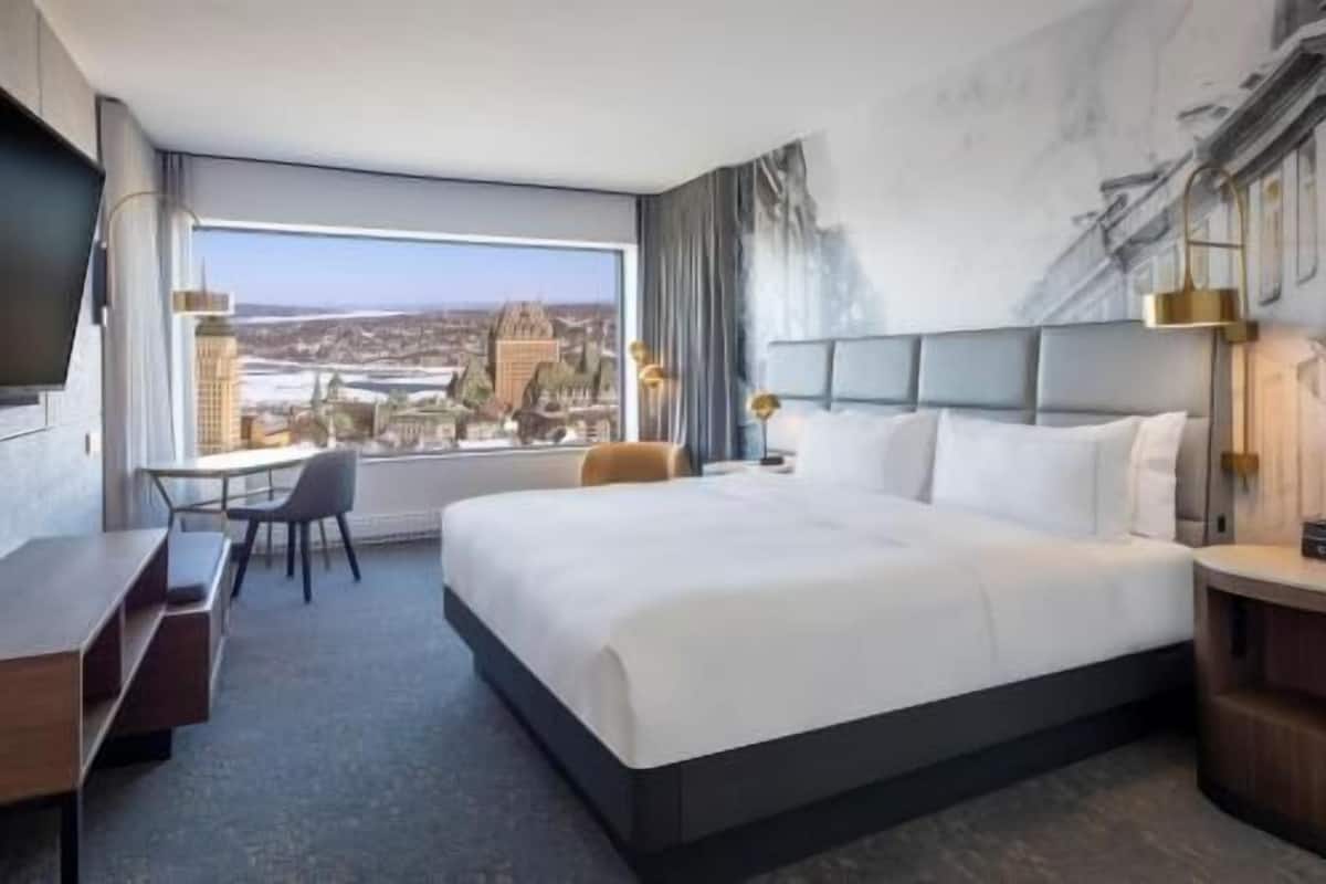 A hotel room with a large bed, a desk, a chair, and a view of a cityscape.