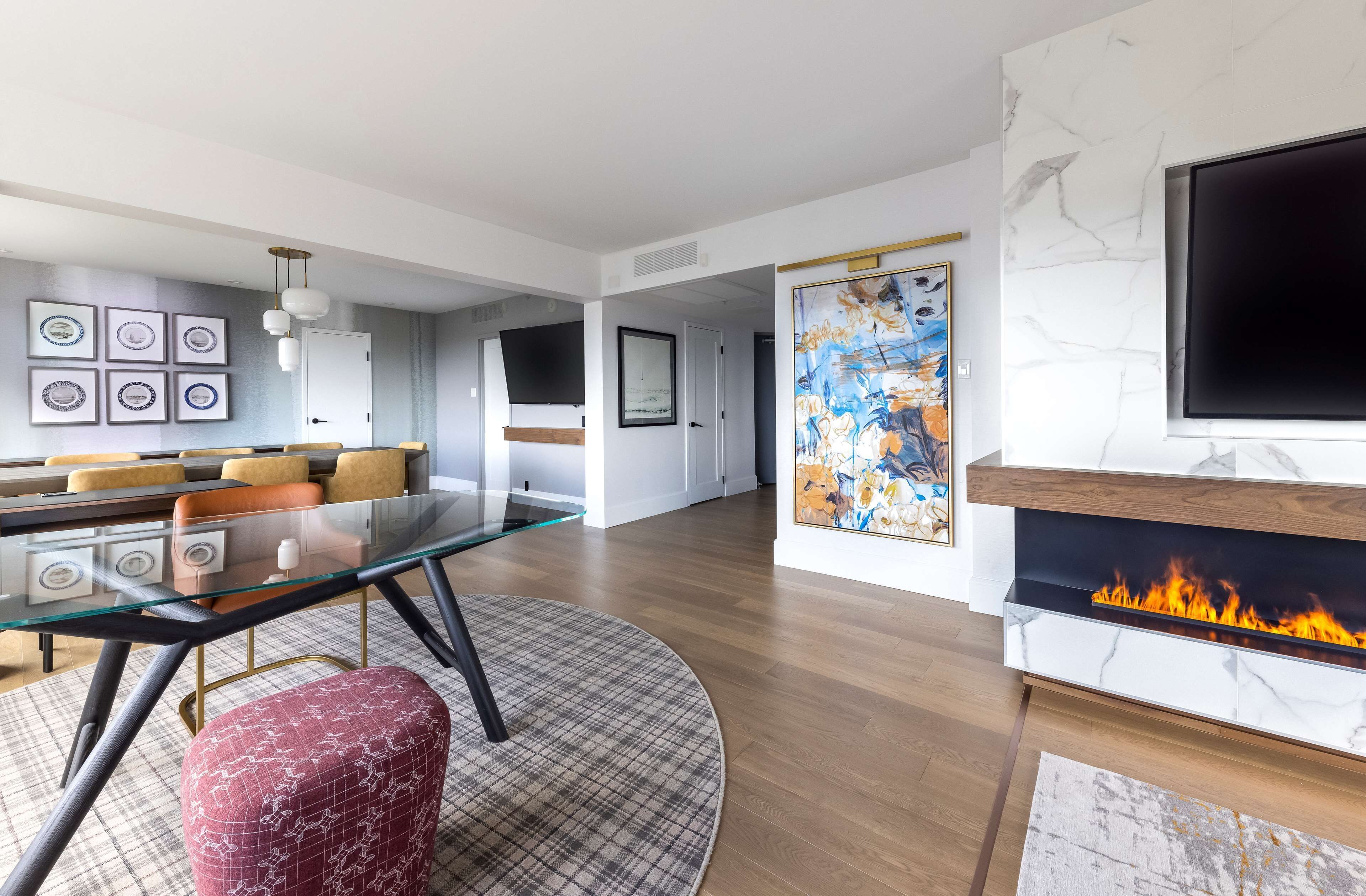 A modern living room with a glass dining table, a fireplace, and a mounted TV.