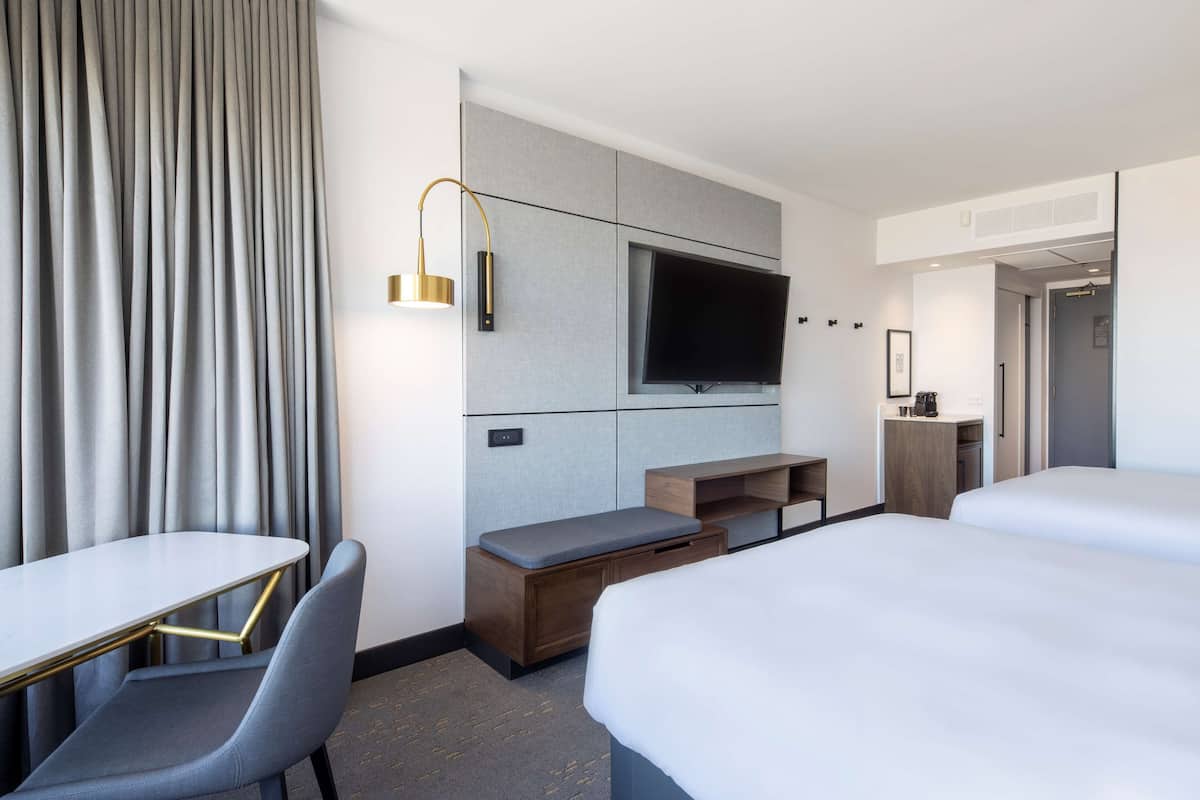 A hotel room with a bed, a desk, a chair, a TV, and a minibar.