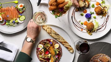 A variety of gourmet dishes on plates, a glass of wine, and a person wearing a watch.