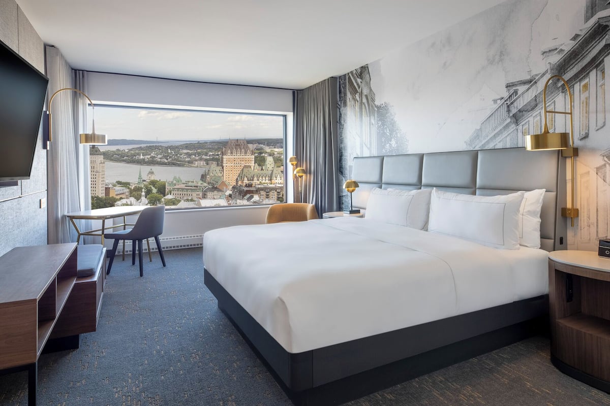 A hotel room with a large bed, a desk, a chair, and a view of a cityscape.