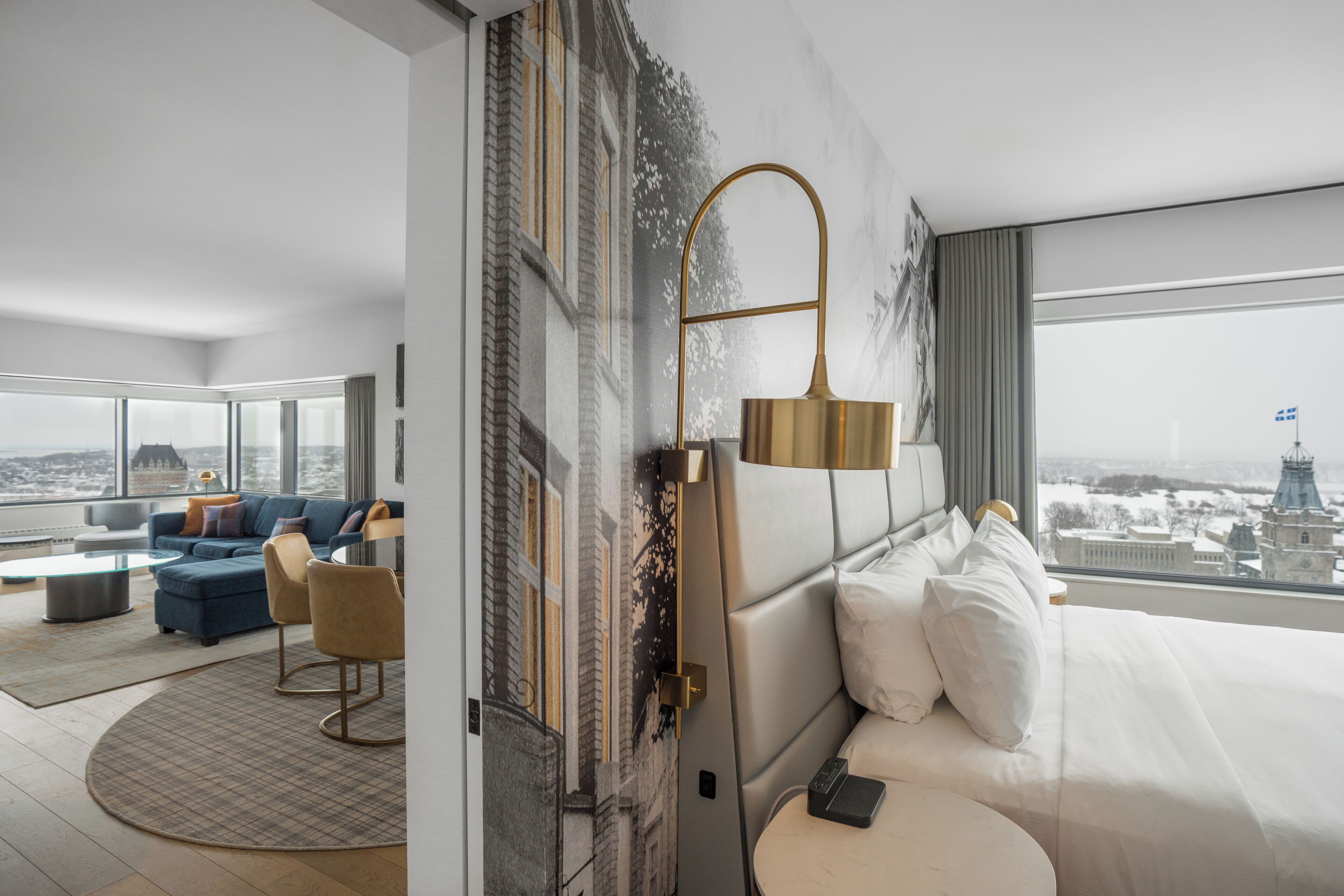 A modern hotel room with a large bed, a sofa, a coffee table, and a view of a cityscape.