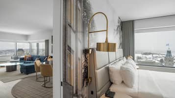 A modern hotel room with a large bed, a sofa, a coffee table, and a view of a cityscape.