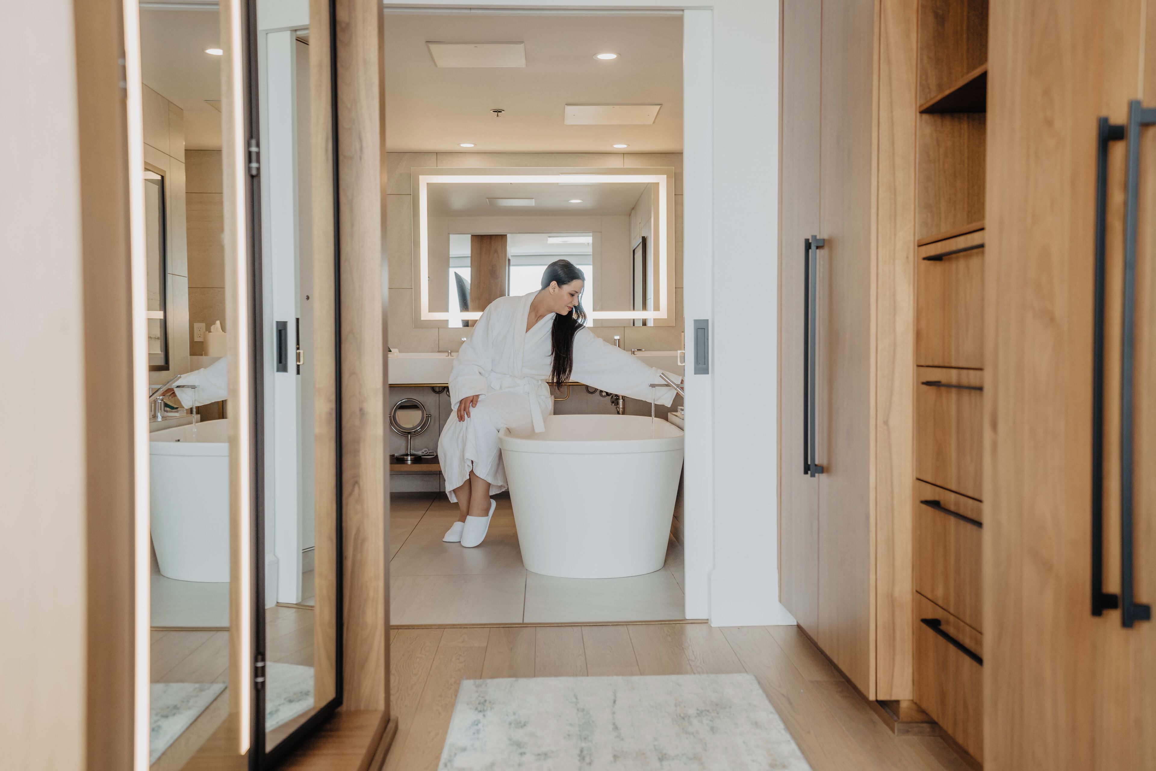 A modern bathroom with a large bathtub, wooden cabinets, and a mirror.