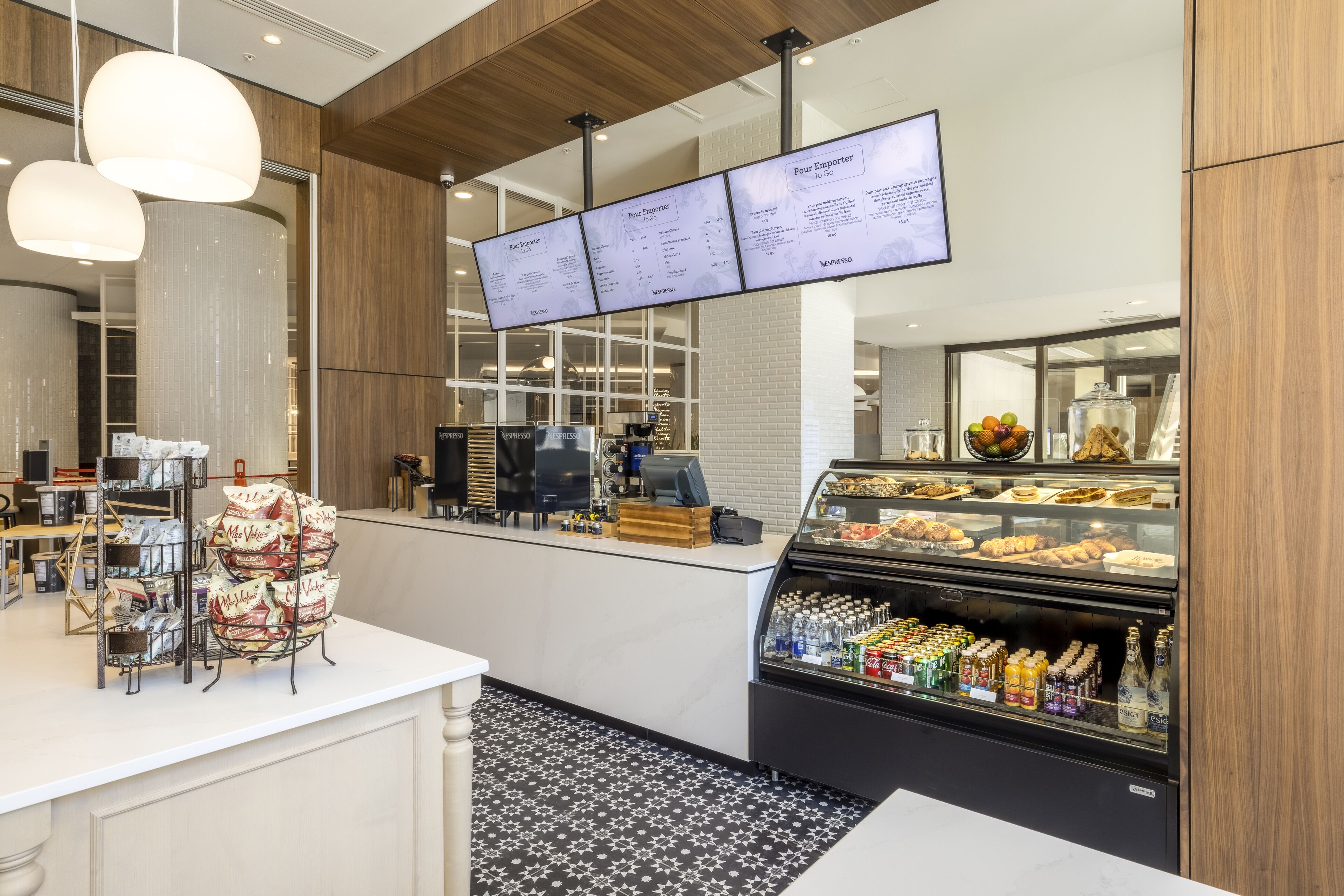 A modern cafe with a self-service counter, menu boards, and a display case with pastries and beverages.
