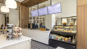 A modern cafe with a self-service counter, menu boards, and a display case with pastries and beverages.