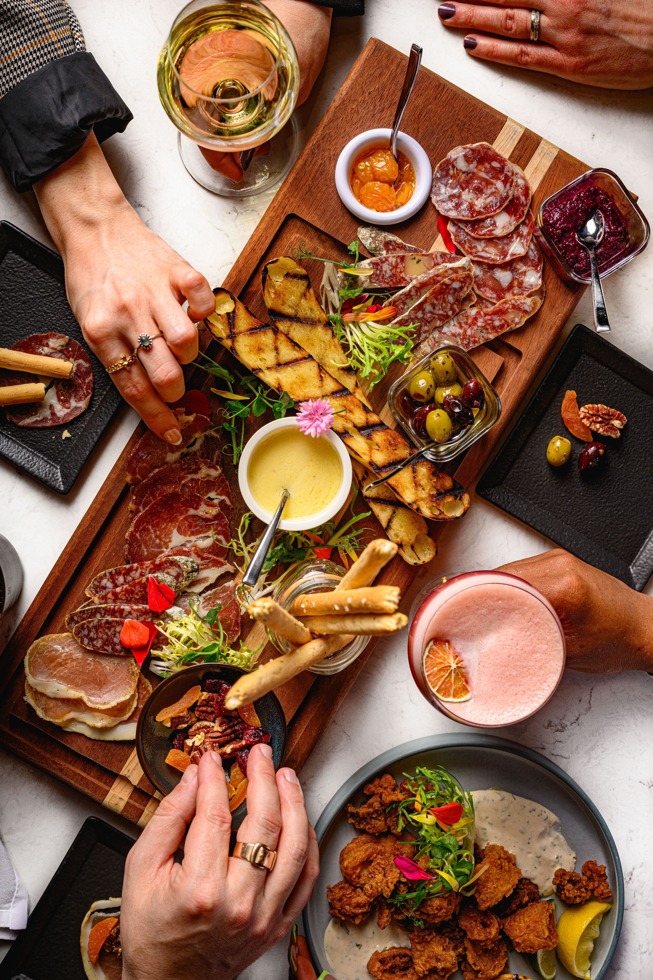 Une variété d’aliments disposés sur une planche en bois, notamment des viandes, des fromages et des légumes, ce qui évoque un buffet ou un repas partagé.