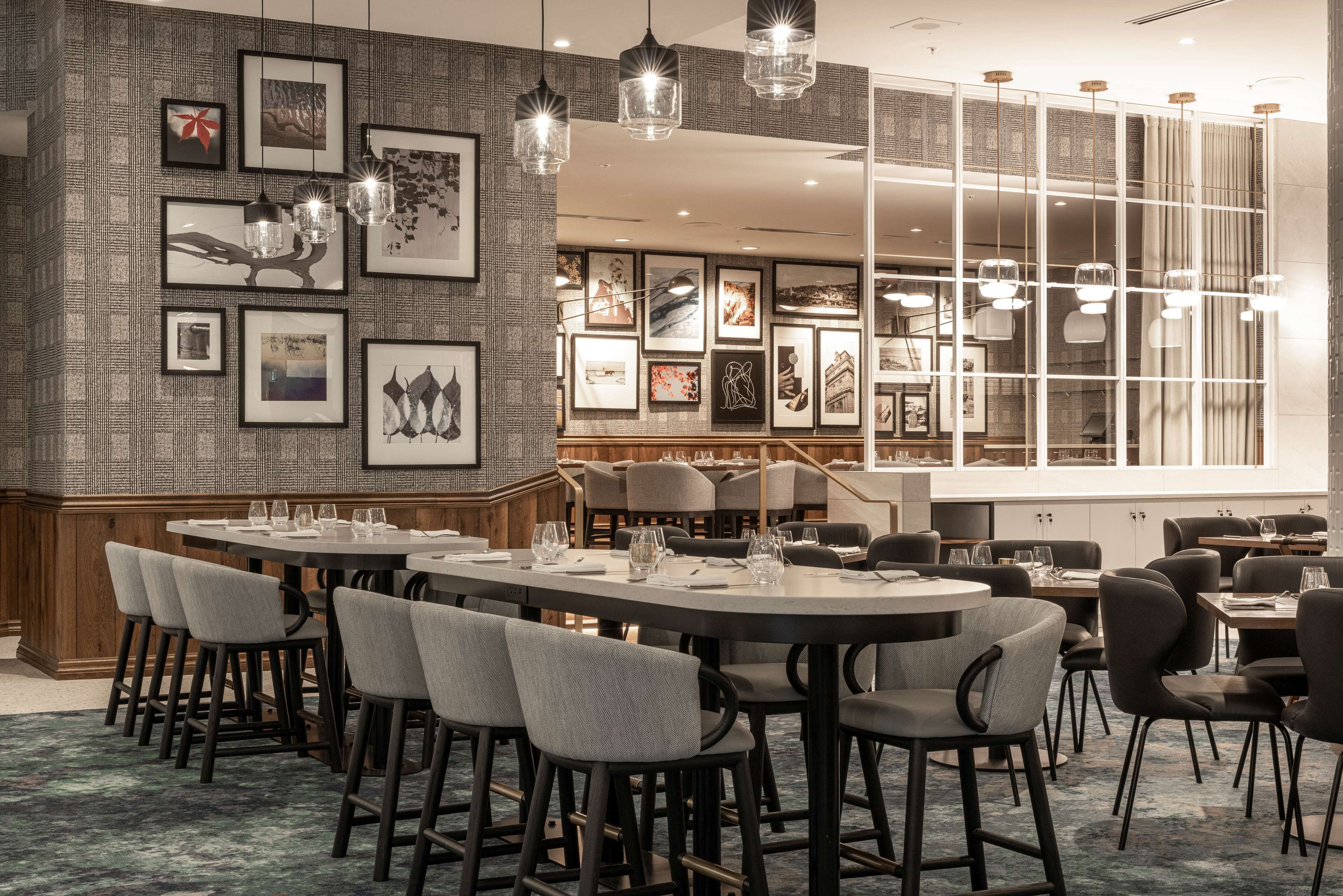 Un comedor moderno con mesas redondas, taburetes de bar y obras de arte enmarcadas en las paredes.