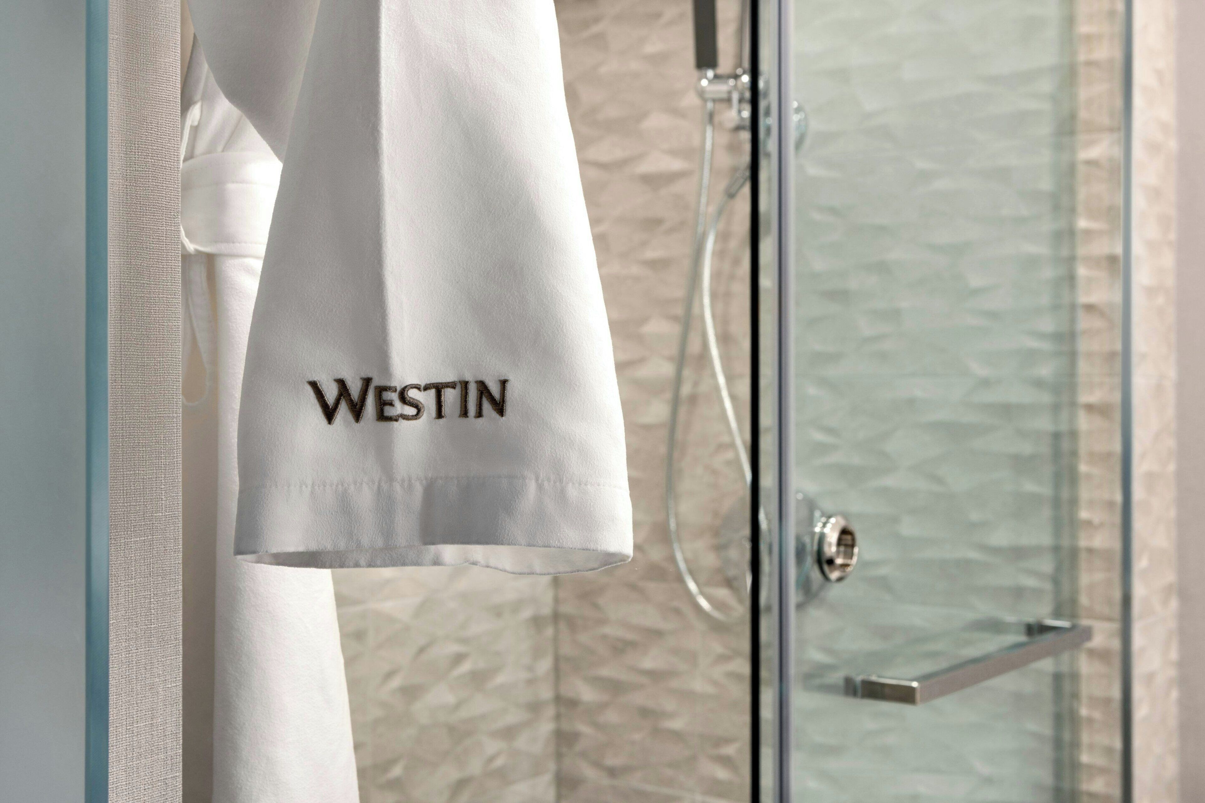 Toalla blanca con el bordado 'WESTIN' colgada en una puerta de ducha de vidrio.