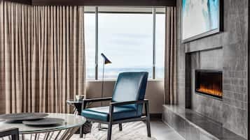 Una sala de estar moderna con chimenea, un ventanal con cortinas, un sillón azul y una mesa de centro de vidrio.
