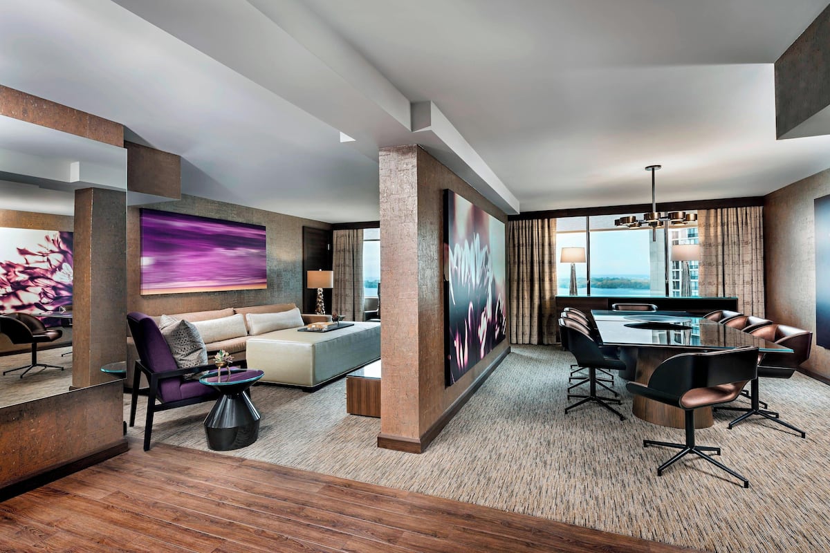 A modern hotel room with a living area, a dining table, and a large window offering a view.