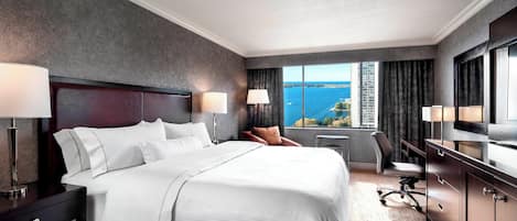 Habitación de hotel con una cama grande, dos mesitas de noche con lámparas, un escritorio con silla y vistas al océano.