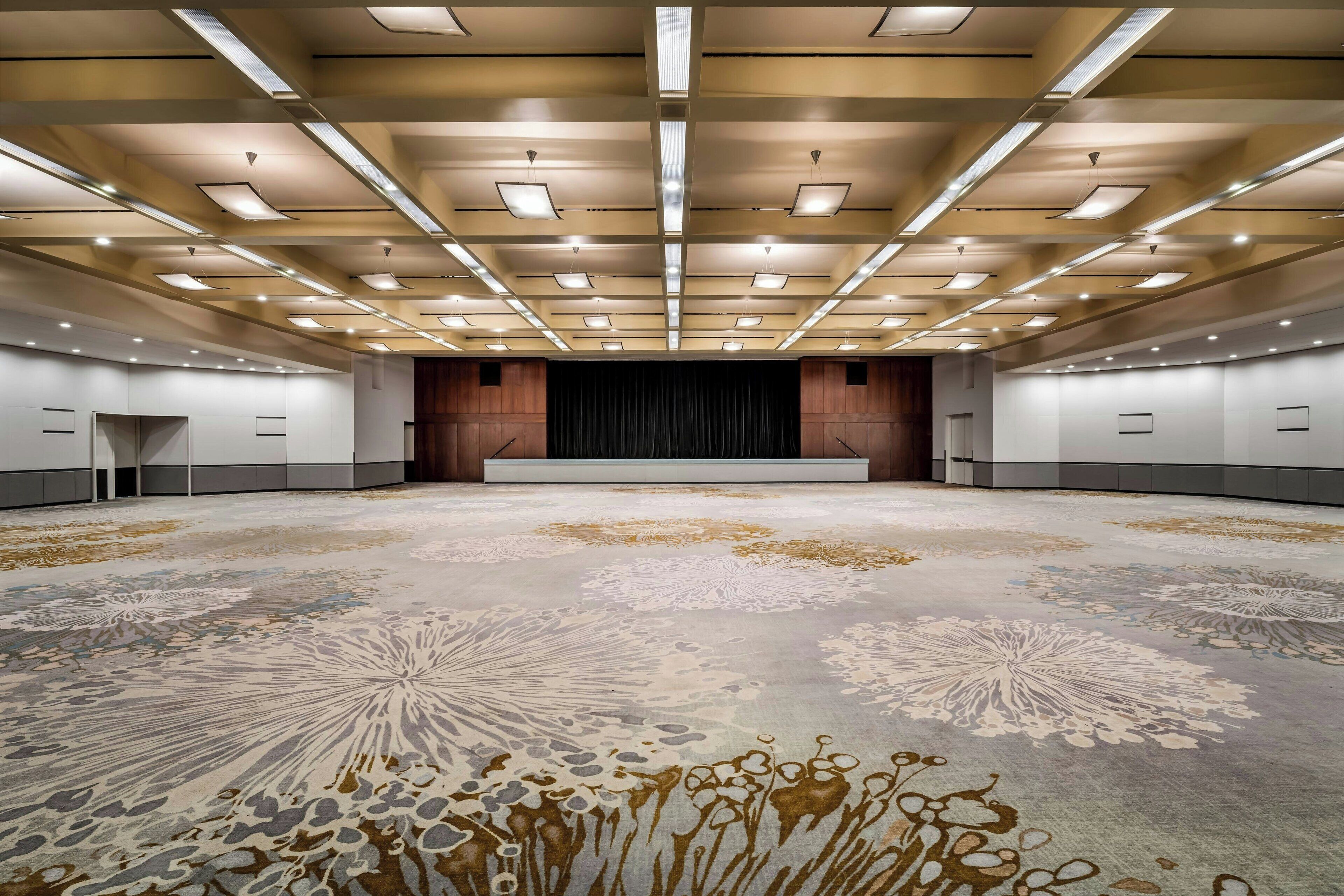 A large conference room with a patterned carpet, recessed lighting, and a stage area.