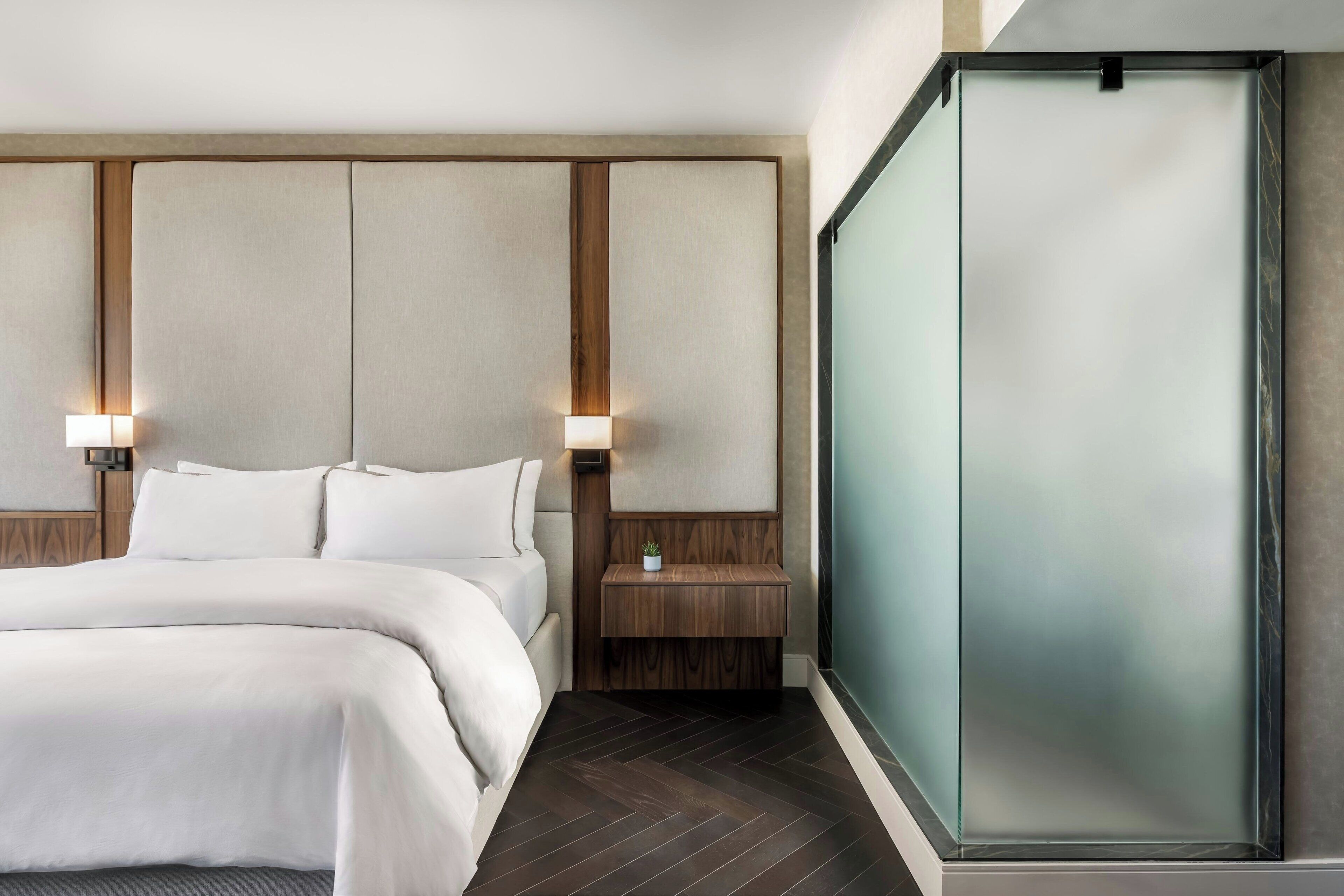 Een moderne hotelkamer met een groot bed, een houten hoofdbord en een wand van glas.