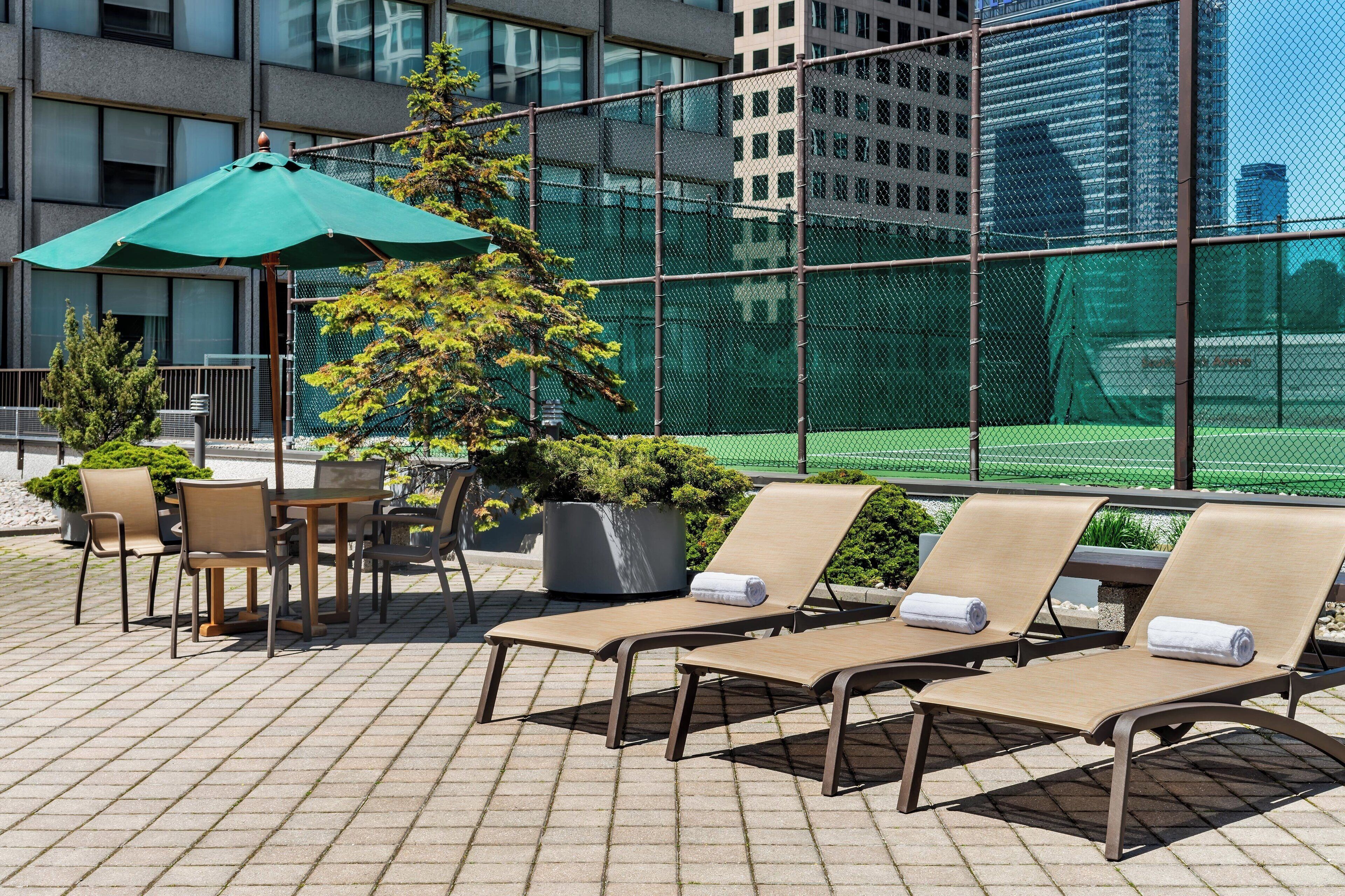 Terraza con sillones, una mesa y sillas, rodeada por una valla verde y macetas con plantas.
