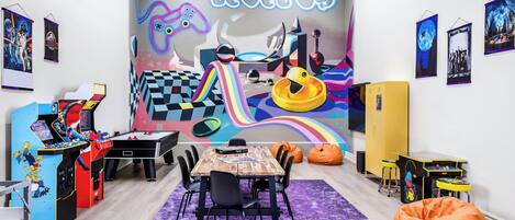 A vibrant children's playroom with a colorful mural, gaming stations, and bean bags.
