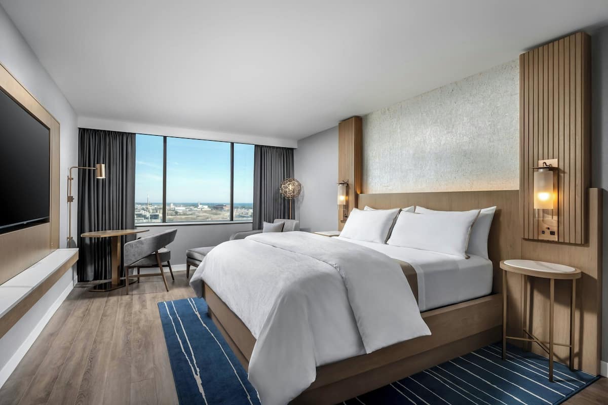 A modern hotel room with a large bed, a desk, a chair, and a TV.