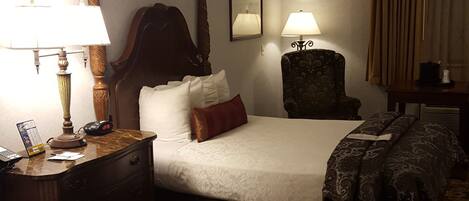 Una habitación de hotel con dos camas, una mesita de noche con lámpara, una silla, un ventilador de techo y una ventana con cortinas.