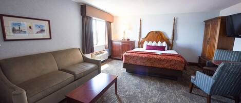 A hotel room with a bed, a sofa, a chair, a table, a TV, and a window with curtains.