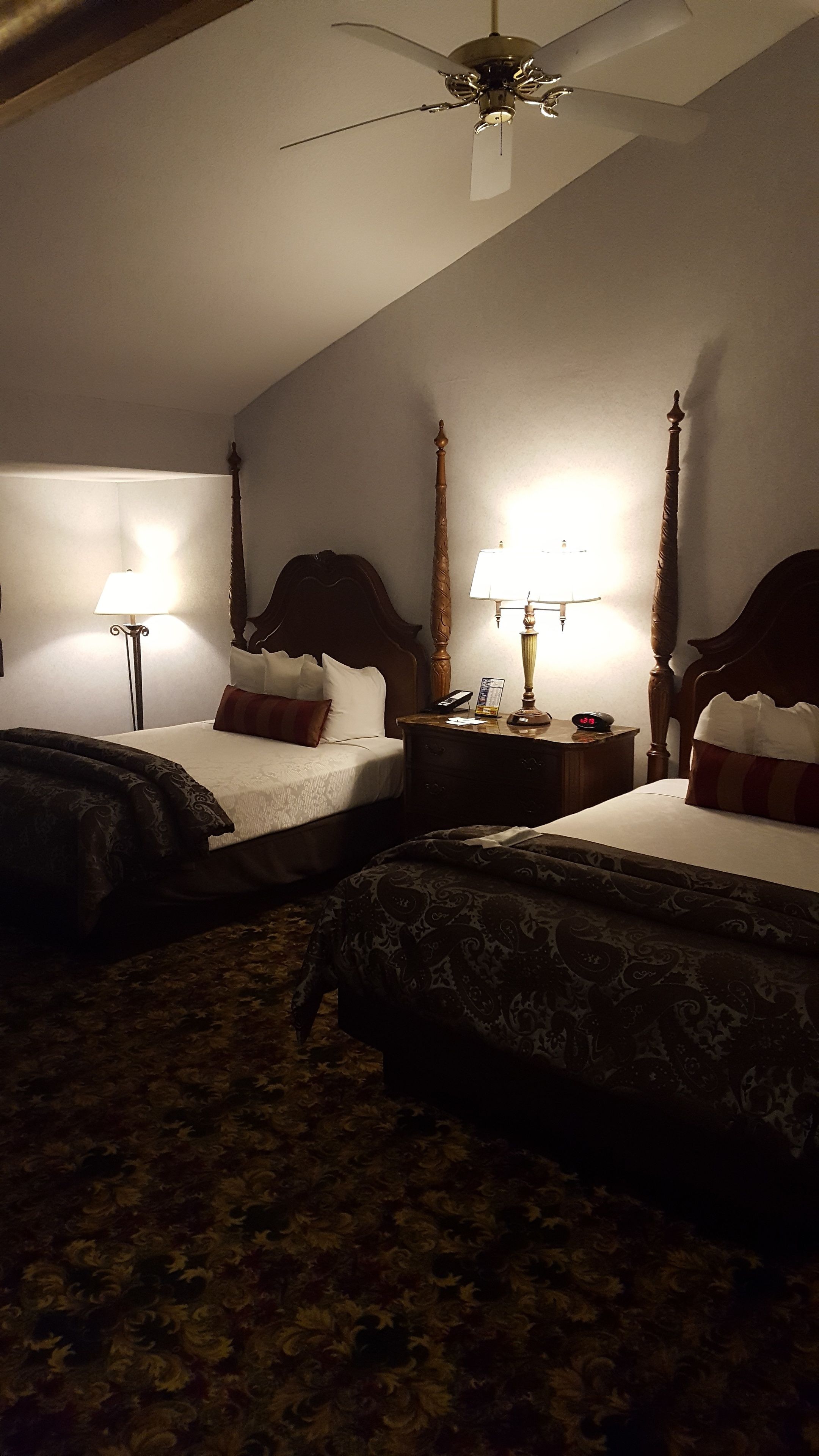 Ein Hotelzimmer mit zwei Betten, einem Deckenventilator und einem Nachttisch mit Lampe.