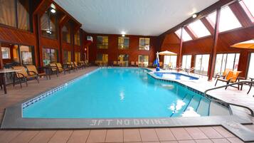 An indoor swimming pool with a tiled floor, wooden walls, and multiple seating areas with chairs and umbrellas.