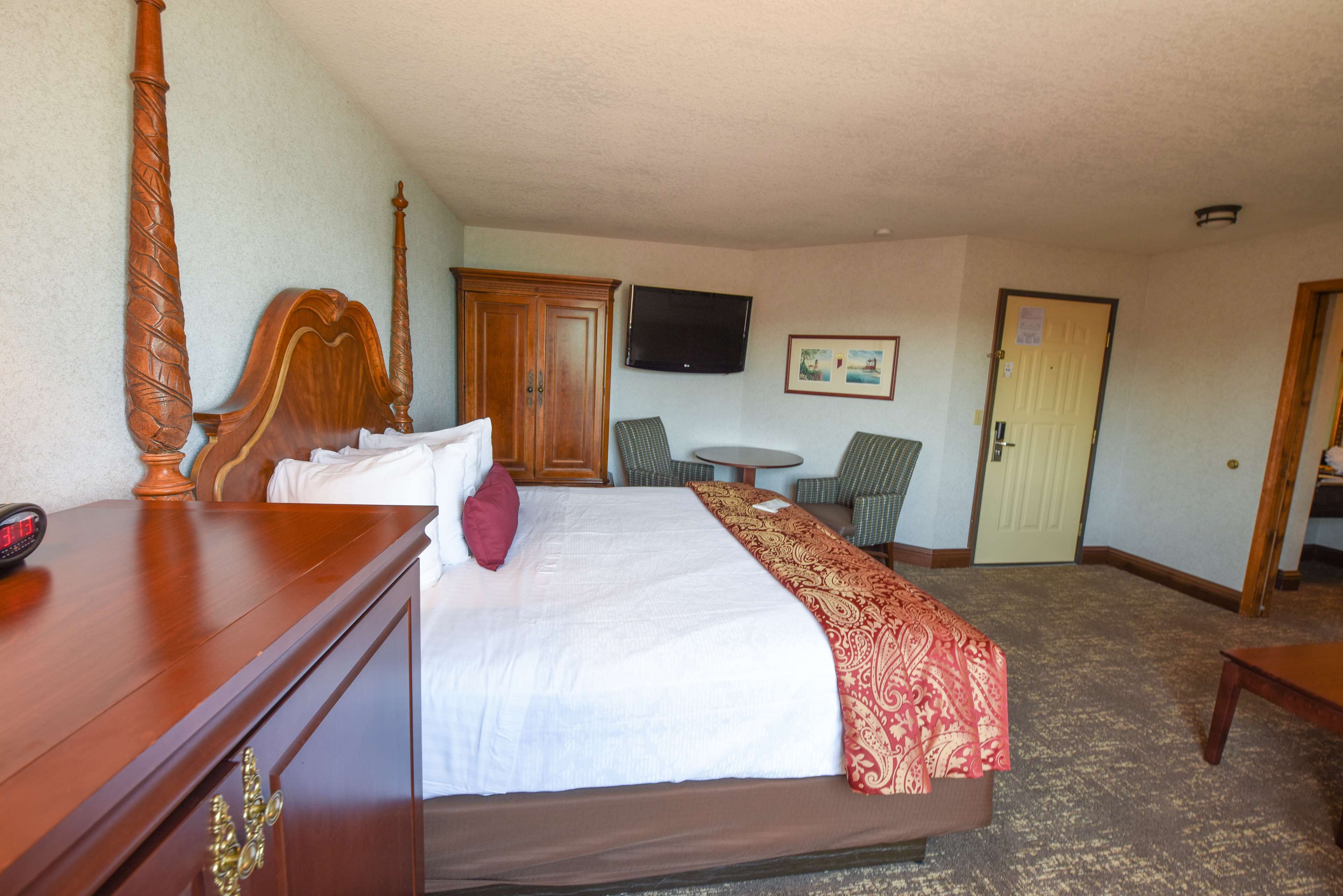 A hotel room with a large bed, a wooden dresser, a television mounted on the wall, and a small round table with chairs.
