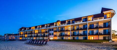 A multi-story hotel with balconies, a beachside location, and a sandy ground area.