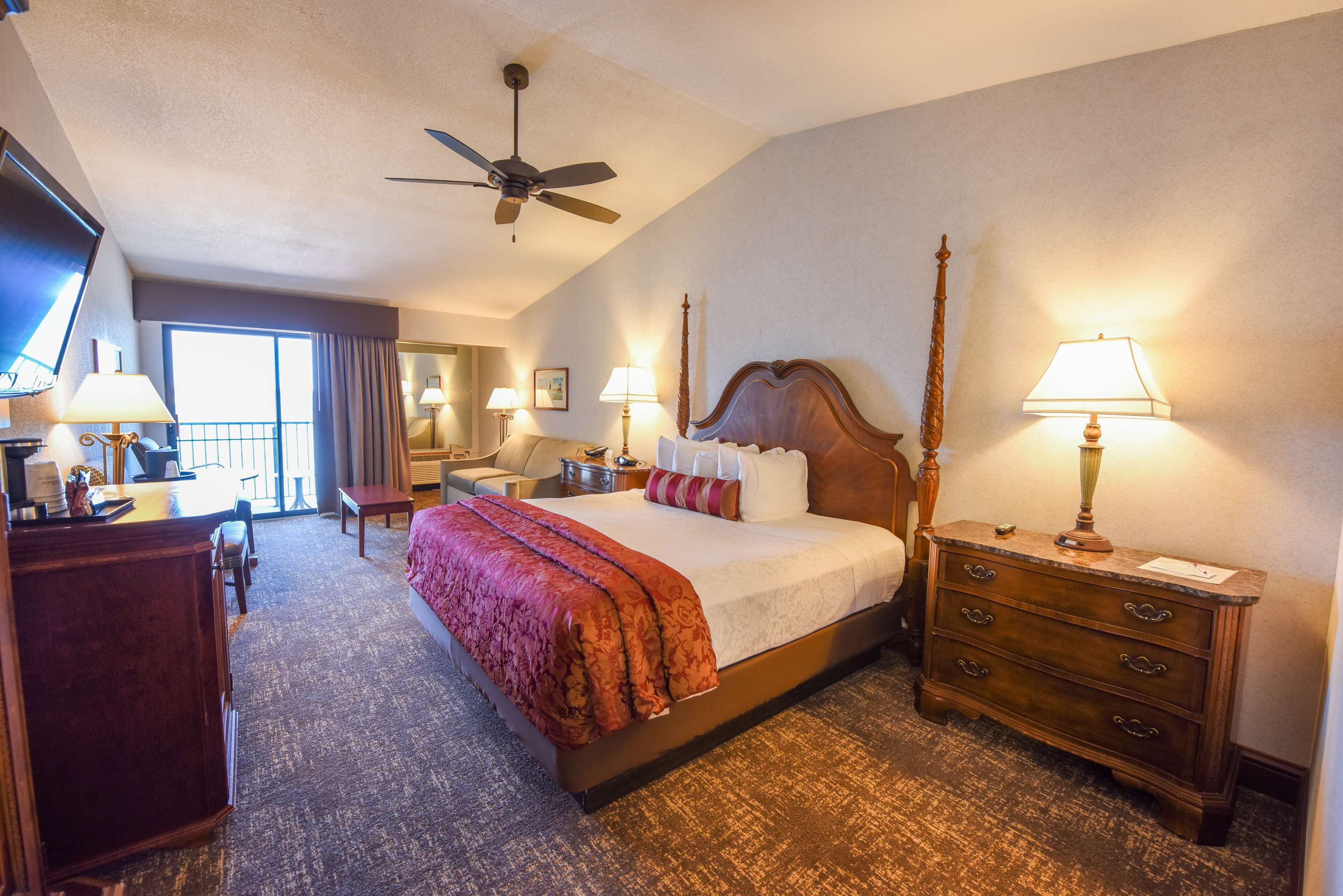 A hotel room with a large bed, a desk, a dresser, and a ceiling fan.