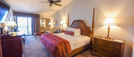 A hotel room with a large bed, a desk, a dresser, and a ceiling fan.