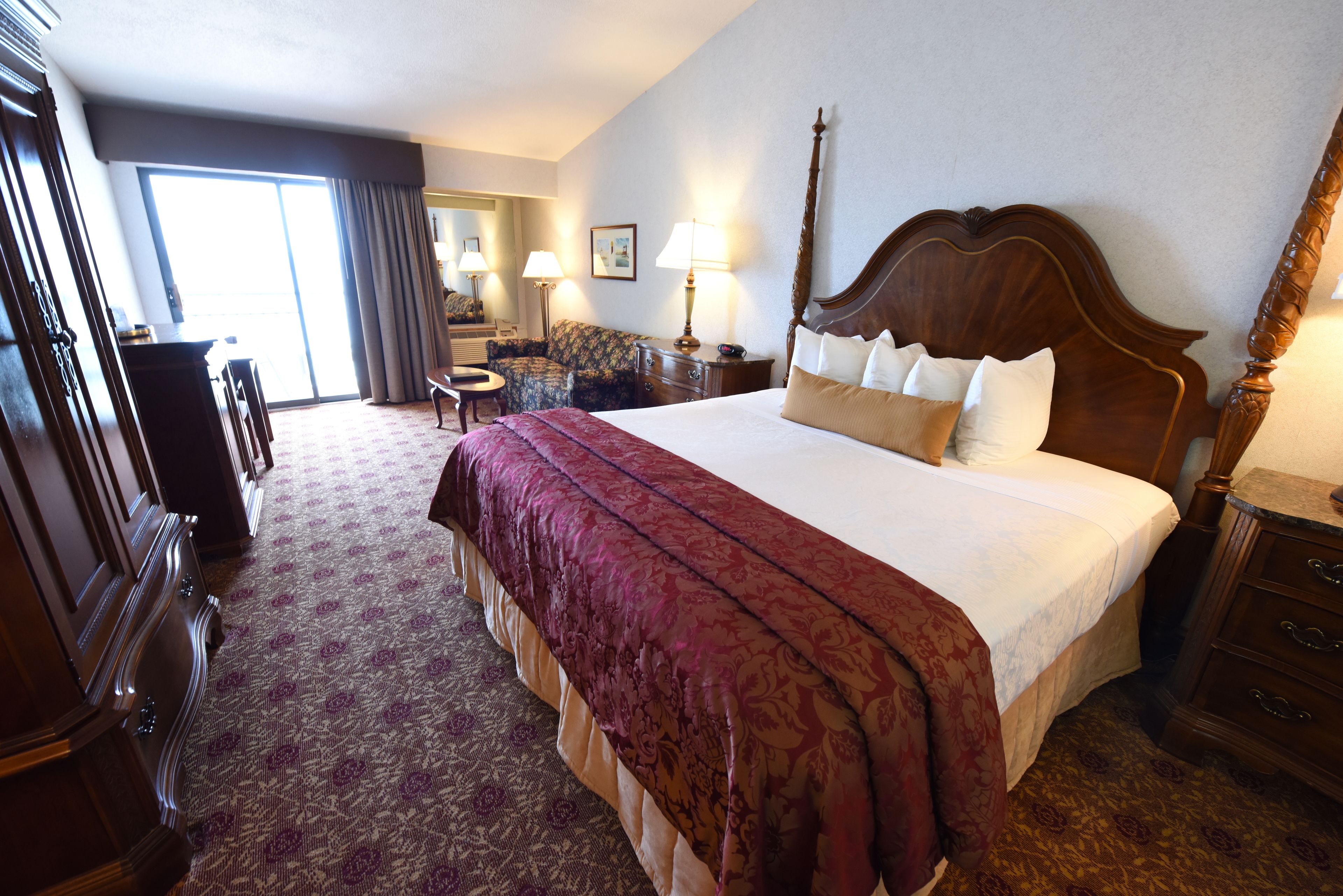 A hotel room with a large bed, a desk, a chair, a dresser, and a view of the outside.